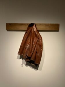 Brown leather jacket with a belt hanging against a neutral wall